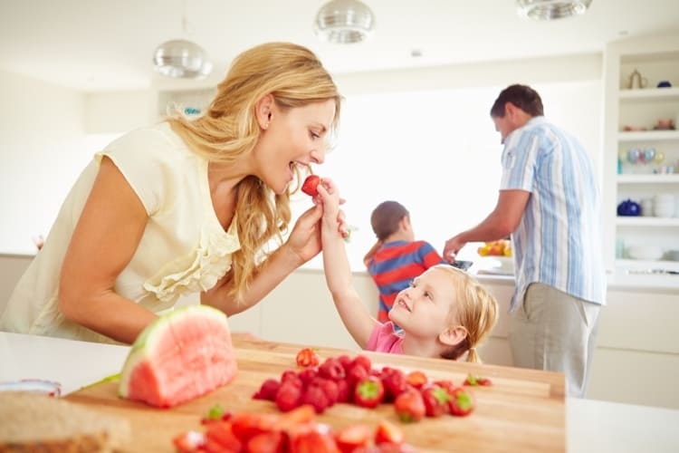 Família feliz a preparar a sobremesa com morangos e melancia.